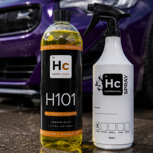 A bottle of Hc H101 all-purpose cleaner and a matching spray bottle displayed side by side in front of a purple car, with wet pavement visible at the bottom.